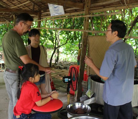 Ông Mười Cương (bên phải) giới thiệu với du khách các sản phẩm ca cao chế biến theo phương pháp truyền thống của nhà vườn ông.