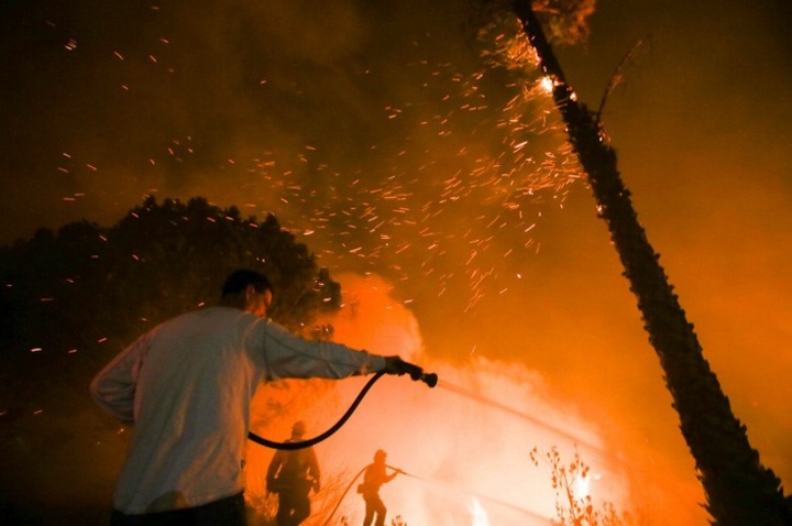 Một người đàn ông hỗ trợ nhân viên cứu hỏa dập tắt ngọn lửa tại Santa Paula, California - Ảnh: AFP