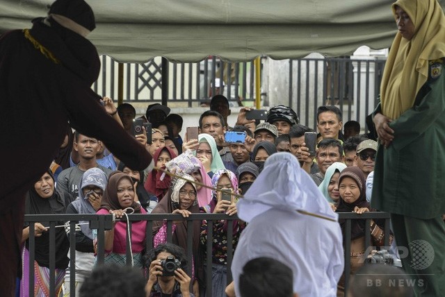 Người dân tỉnh Aceh (Indonesia) xem bà Tjia Nyuk Hwa, 45 tuổi, một người theo đạo Cơ đốc, bị đánh bằng roi công khai ngày 27/2/2018 vì vi phạm luật Hồi giáo Sharia khắt khe khi chơi một trò chơi giải trí của trẻ em - Ảnh: AFP
