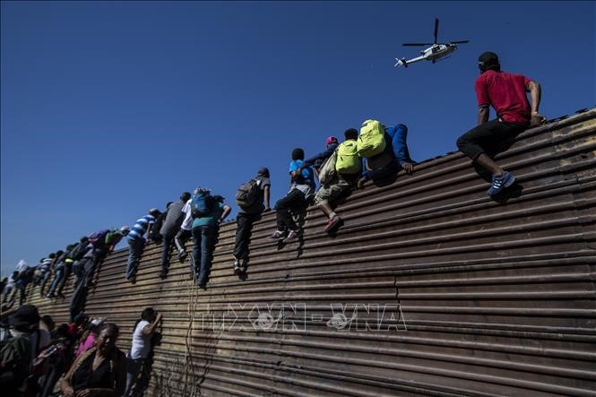 Người di cư trèo qua bức tường biên giới Mexico-Mỹ, gần cửa khẩu El Chaparral ở Tijuana, bang Baja California, Mexico. Ảnh tư liệu: AFP/TTXVN
