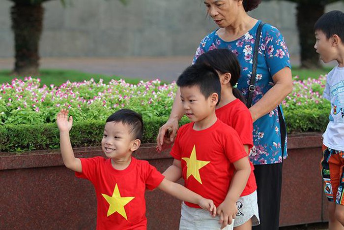 Các em nhỏ mặc áo in hình cờ Tổ quốc rạng rỡ cùng cha mẹ đi thăm lăng Bác.
