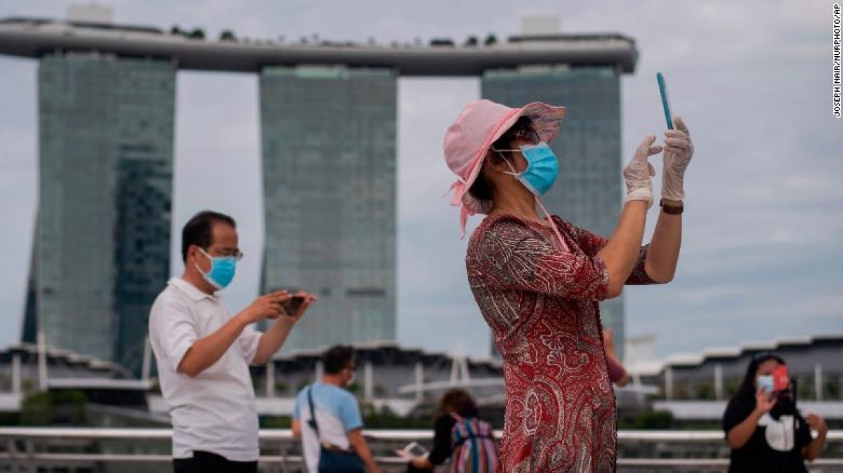Một người phụ nữ đeo khẩu trang và găng tay chụp hình ở Vịnh Marina, Singapore ngày 1/8. Ảnh: CNN
