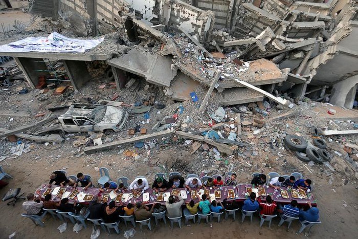 Trong tháng lễ Ramadan, một nhóm người dân Palestine tập trung ăn uống cạnh đống đổ nát của tòa nhà bị phá hủy sau các đợt không kích của Israel tại Dải Gaza.