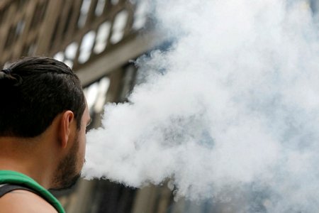 Một người đàn ông sử dụng thuốc lá điện tử khi đi bộ tại Broadway, New York, Mỹ. Ảnh: Reuters