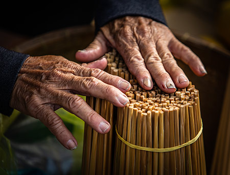 Một cụ bà đã ngoài 60 tuổi, với bó đũa tre sản xuất tại nhà, bày bán tại chợ.
