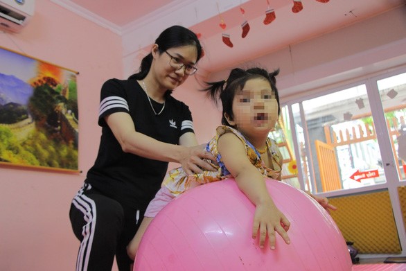 Chị Lan Anh cùng con gái tập các bài tập phục hồi chức năng tại trung tâm chăm sóc đặc biệt cho trẻ - Ảnh: HÀ THANH